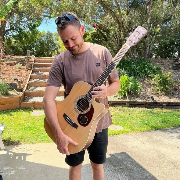 Joshua holding an acoustic guitar in a garden